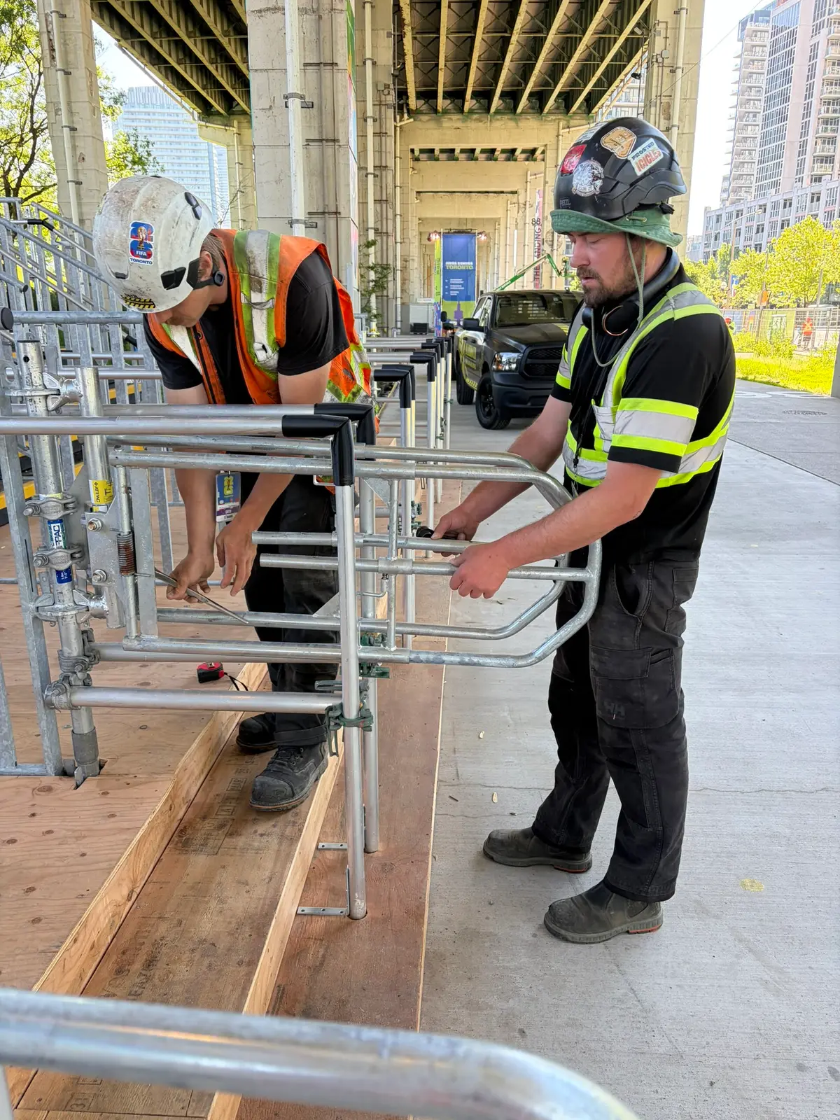 Two Mammoth crew members installing self-closing scaffold gates on an accessible ramp under the Gardiner Expressway