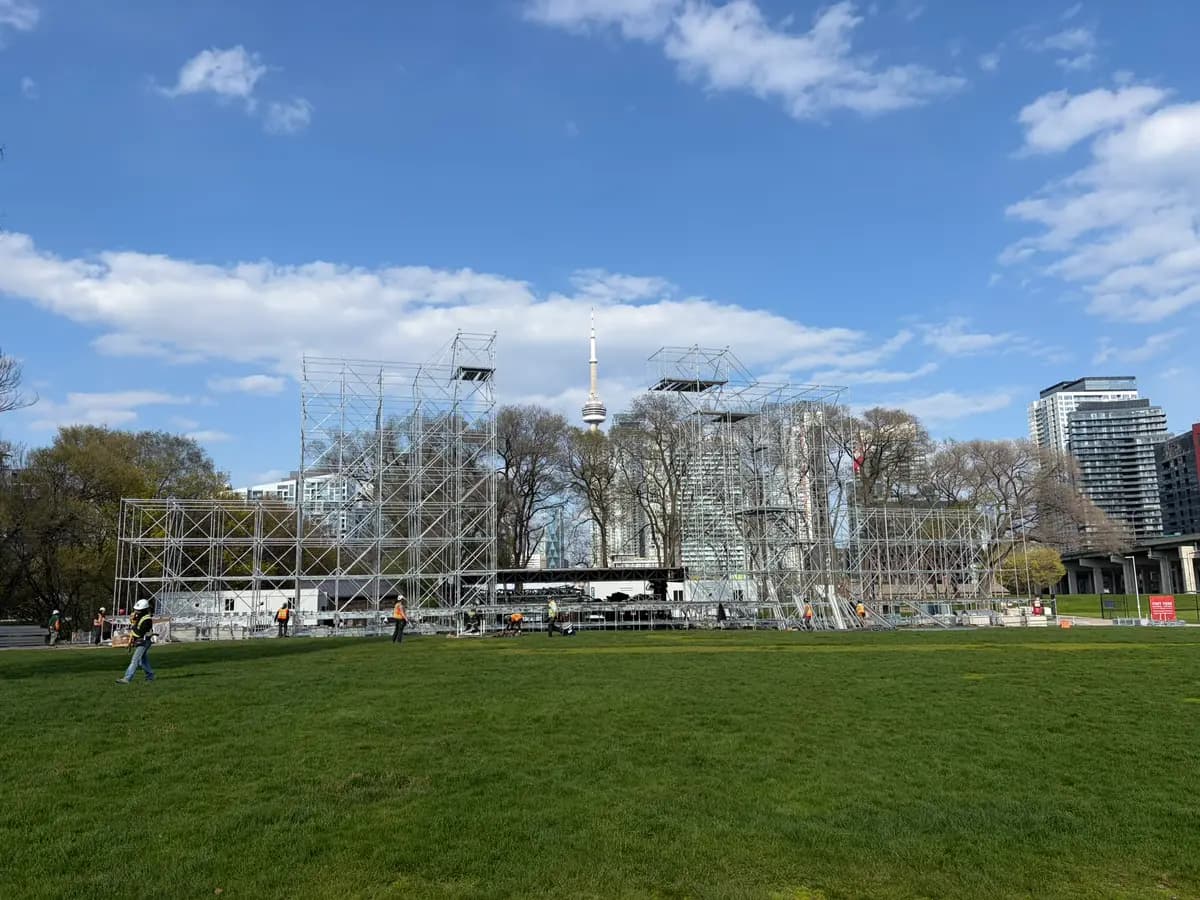 Event stage scaffold towers at Fort York under blue skies with the CN Tower rising between them