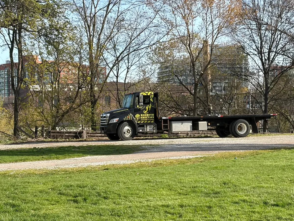 Mammoth Erection branded flatbed truck staged on a gravel path at a Toronto park event site in warm evening light