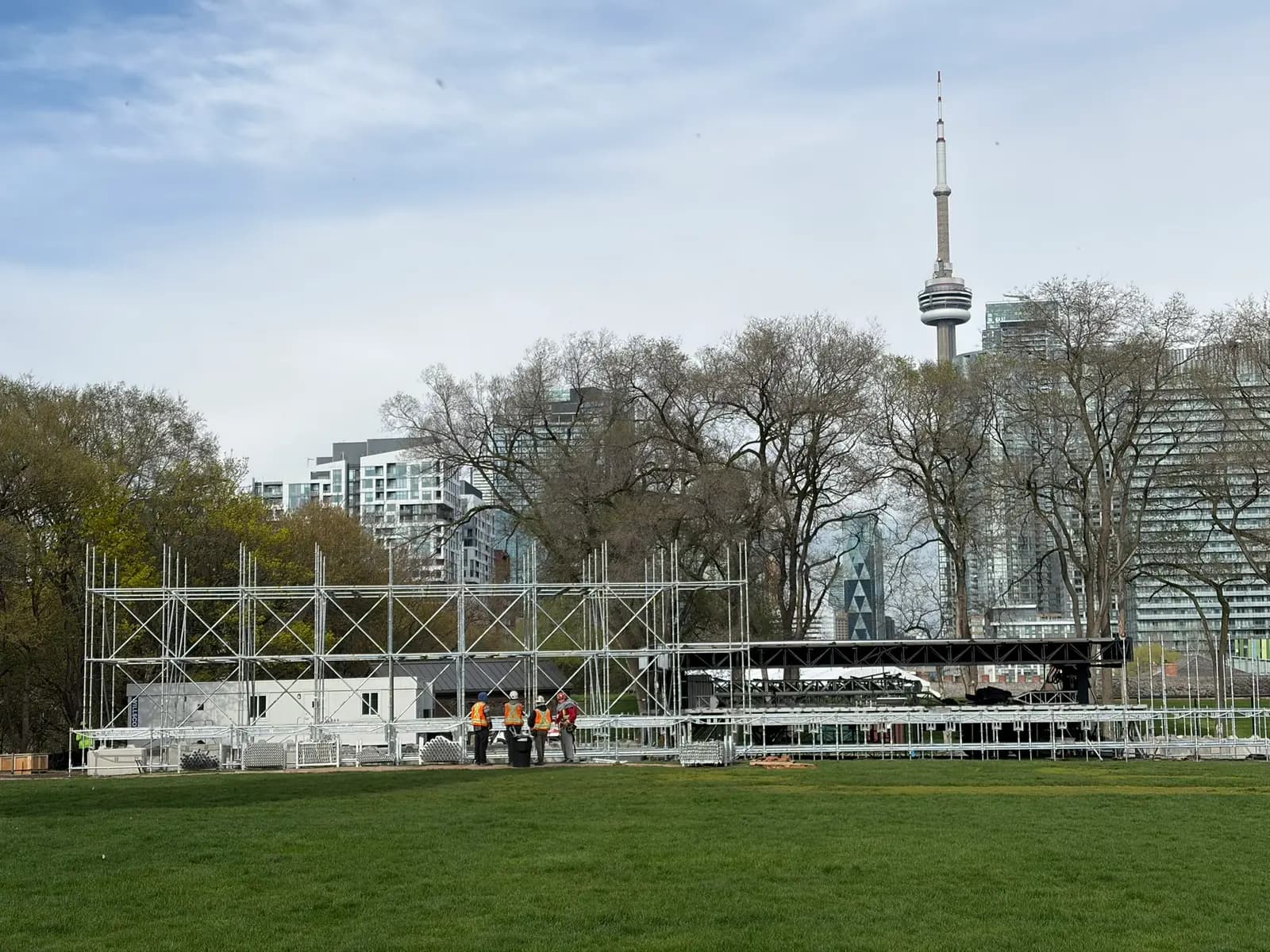 Festival main stage scaffold towers rising at Fort York with the CN Tower and downtown Toronto behind.