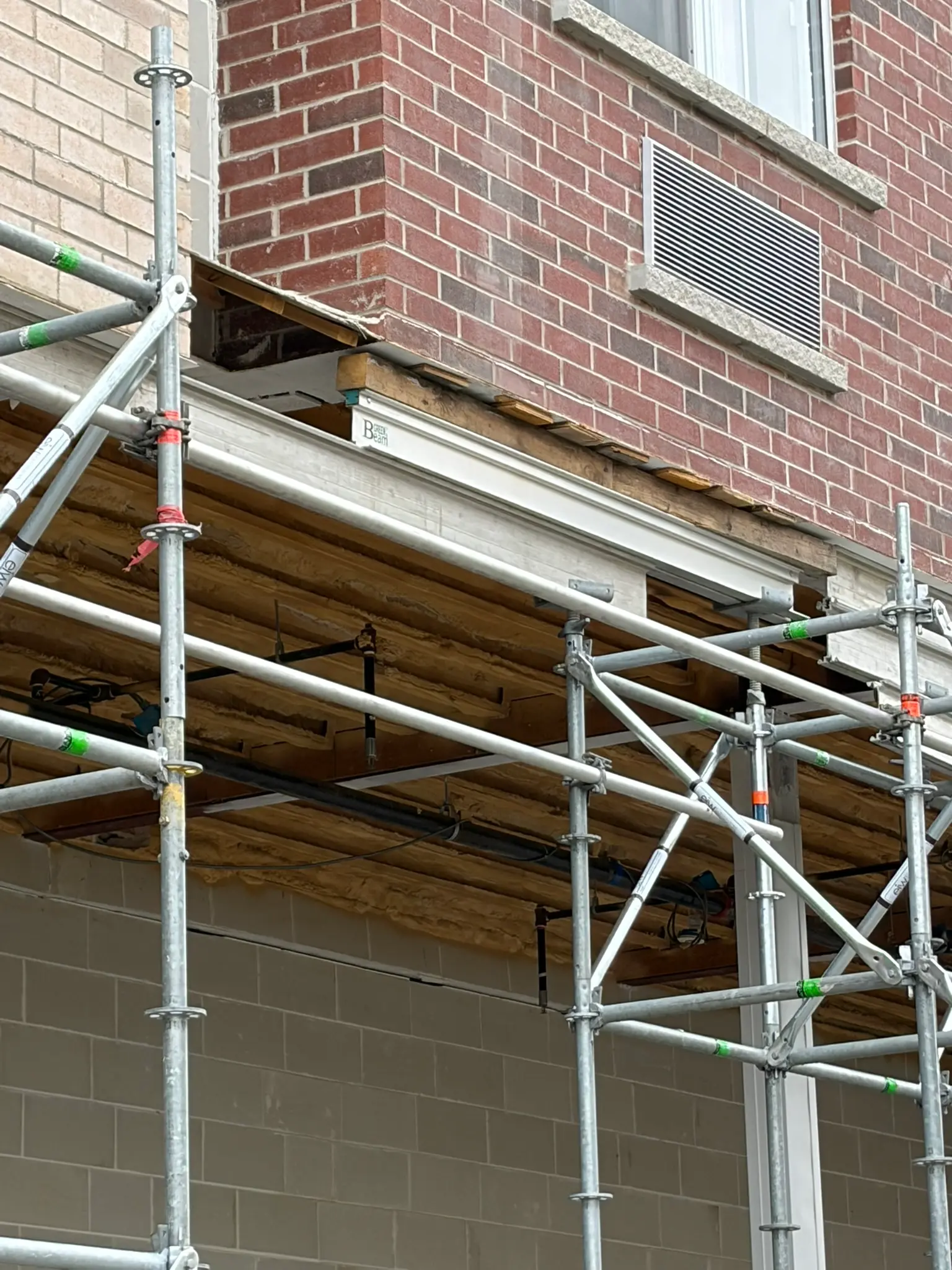 Scaffold shoring posts and engineered beams supporting a brick building canopy with exposed joists during restoration