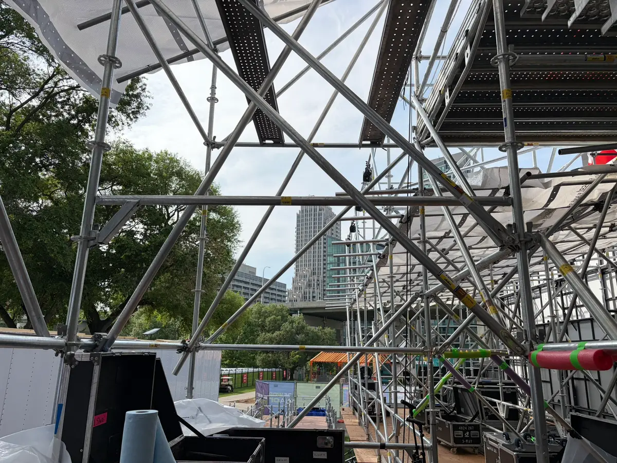View through the criss-crossing braces and decks of an event stage scaffold toward the downtown Toronto skyline