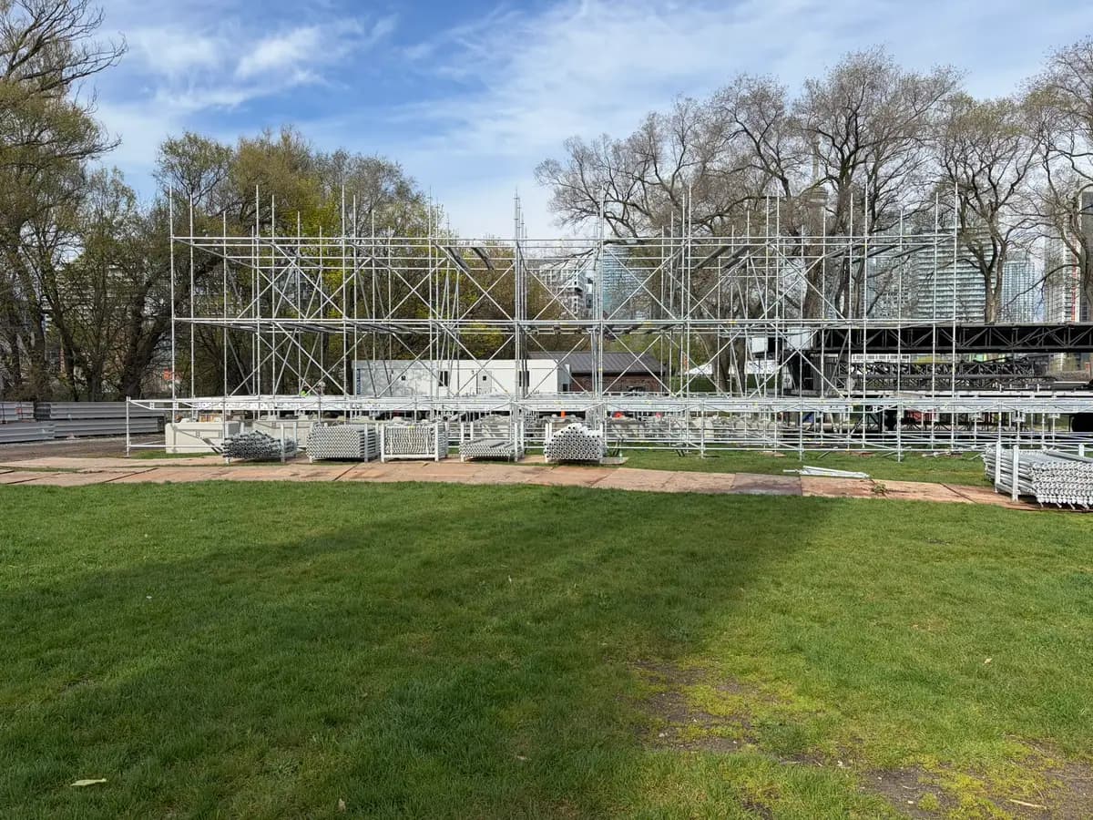 Braced system scaffold towers for a festival stage standing against a blue spring sky at Fort York.
