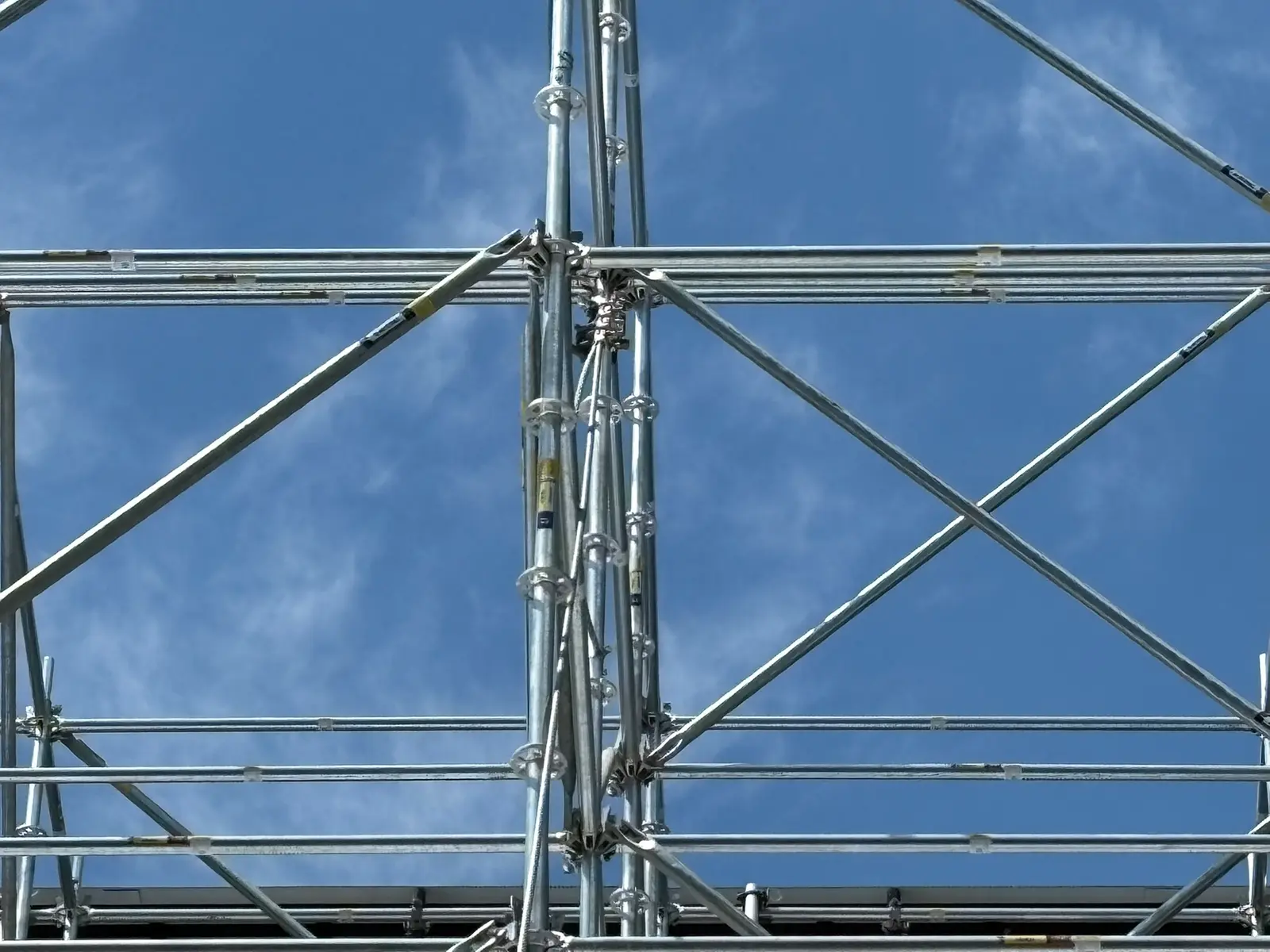 Looking up through galvanized system scaffold standards and cross-bracing against a clear blue sky
