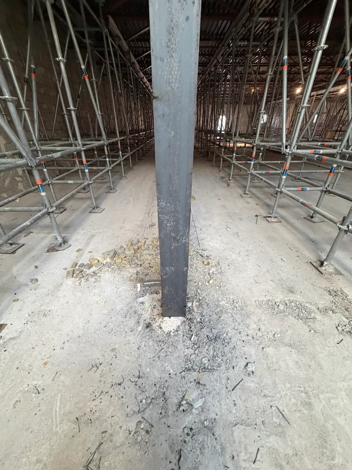 Symmetrical rows of shoring towers flanking a steel column beneath a warehouse roof deck