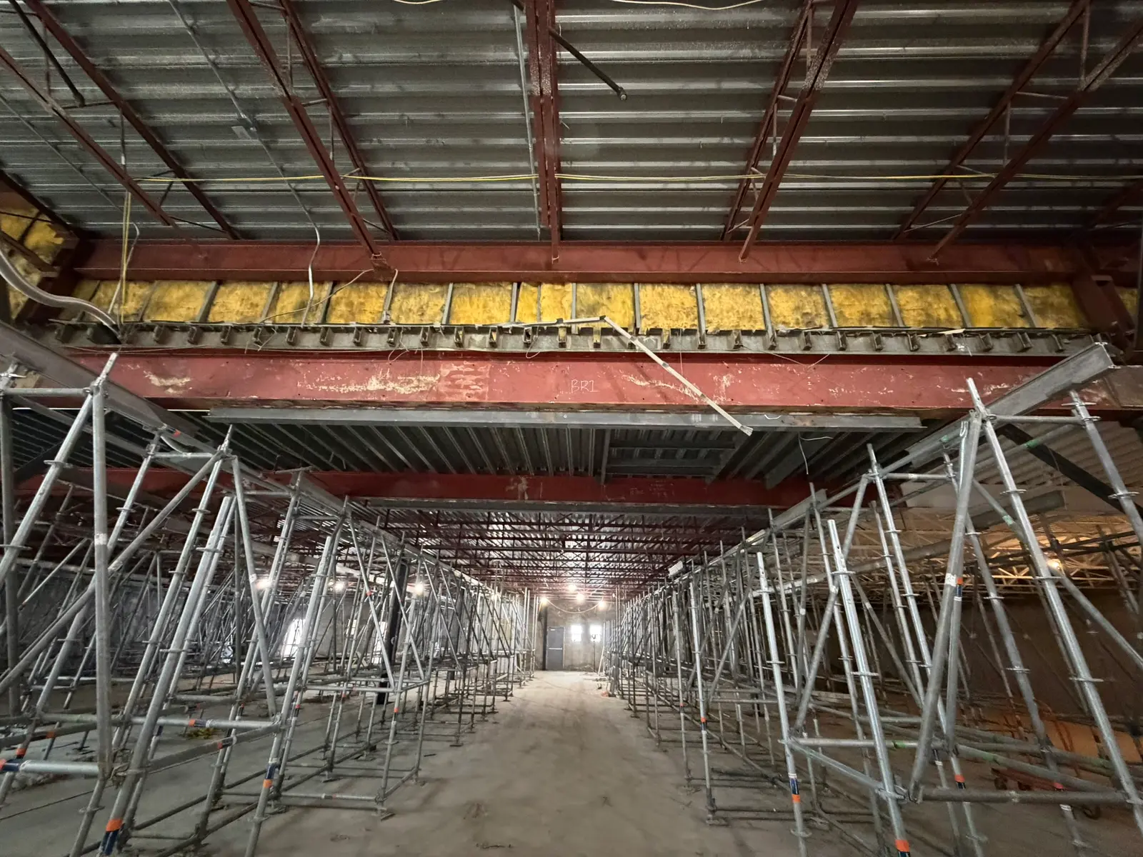A vast field of system scaffold shoring towers supporting new structural steel and roof deck across a full-building commercial renovation.