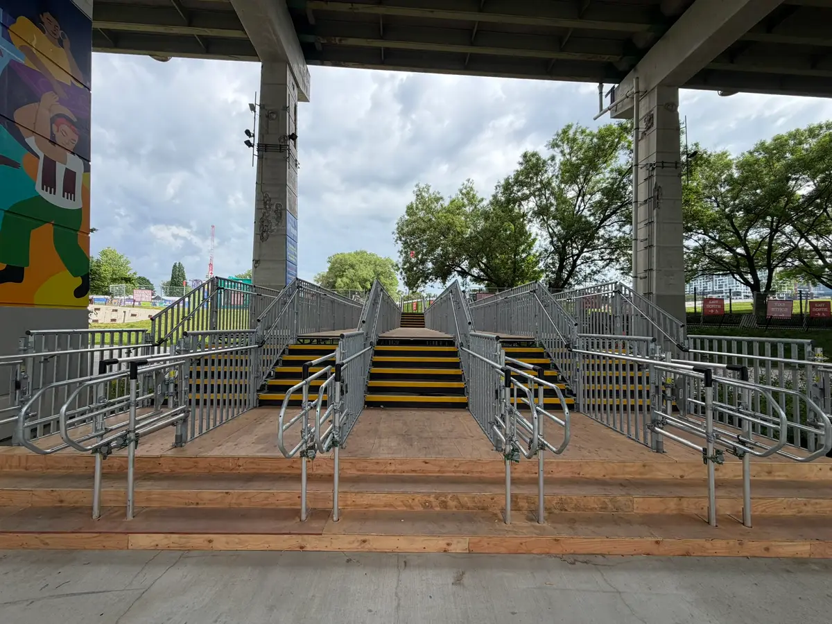 Symmetrical temporary stair and queuing system with yellow-nosed treads built under an elevated expressway for event access.
